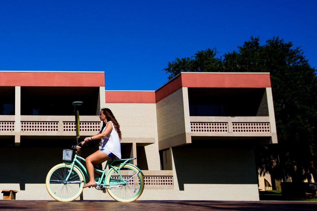 girl riding bike in front of NCF dormitory.